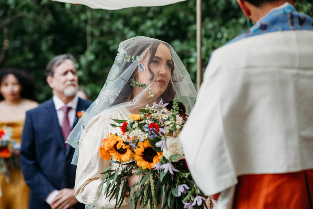 Close up photo of bride with veil over face looking at groom