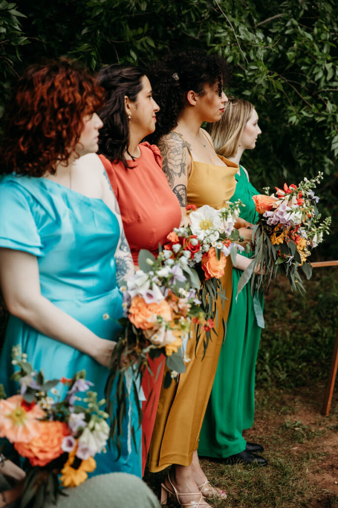Bridesmaids in multicolored dresses watching wedding ceremony