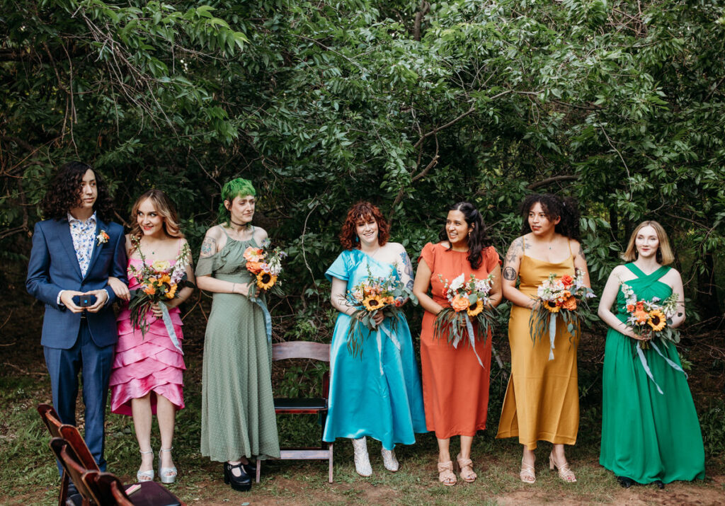 Bridesmaids in multicolored dresses standing in a line holding bouquets