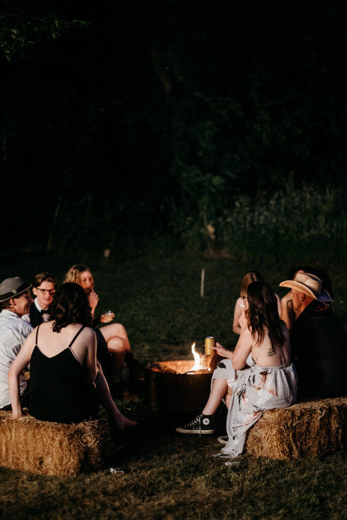 Wedding guests sitting on hay bales around small fire