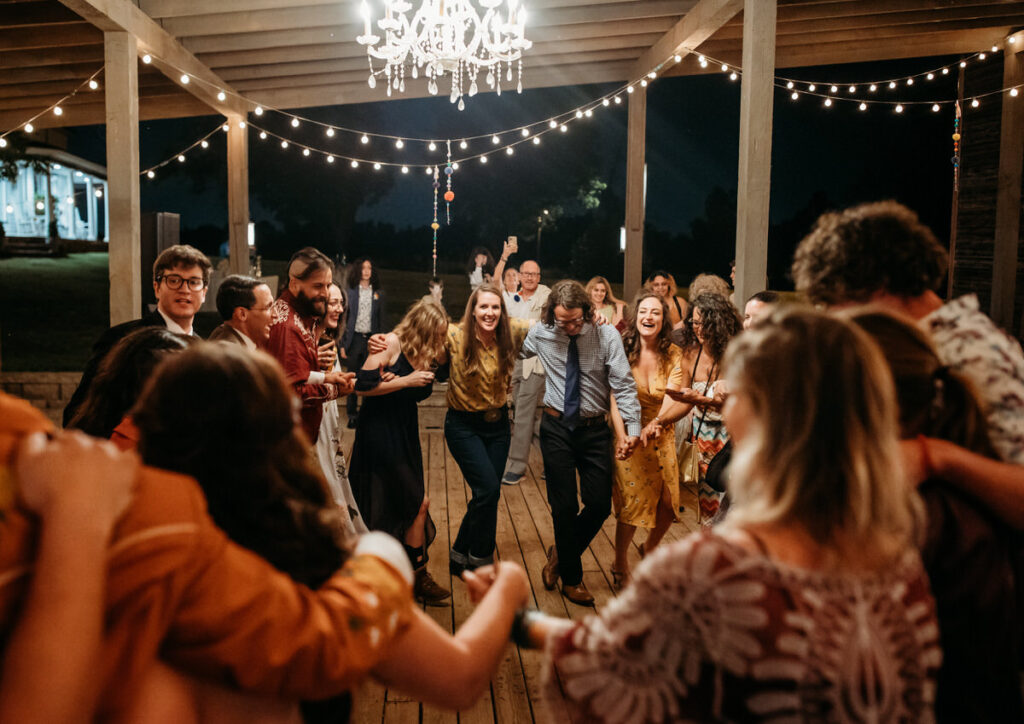 Wedding guests dancing joyously in a pavilion adorned with string lights, creating a festive atmosphere at the evening reception