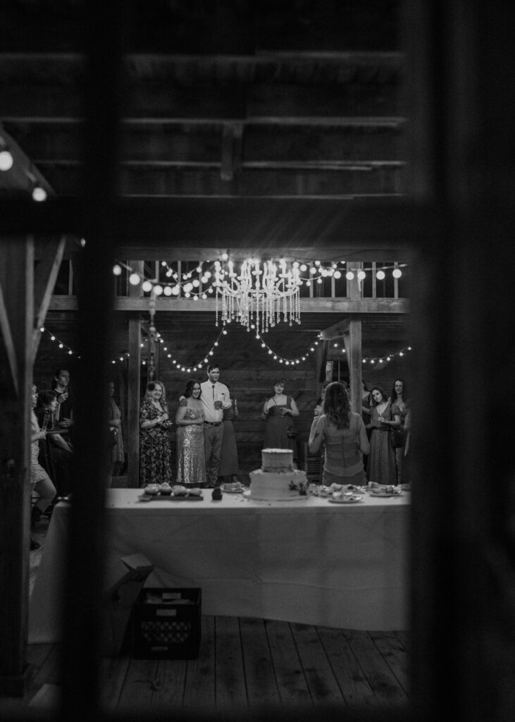 Black and white photo of wedding reception table with string lights in barn