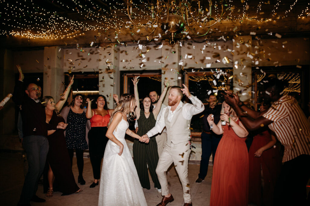 A vibrant wedding celebration, with guests joyously throwing confetti as the couple holds hands and runs through, encapsulating a festive and happy occasion