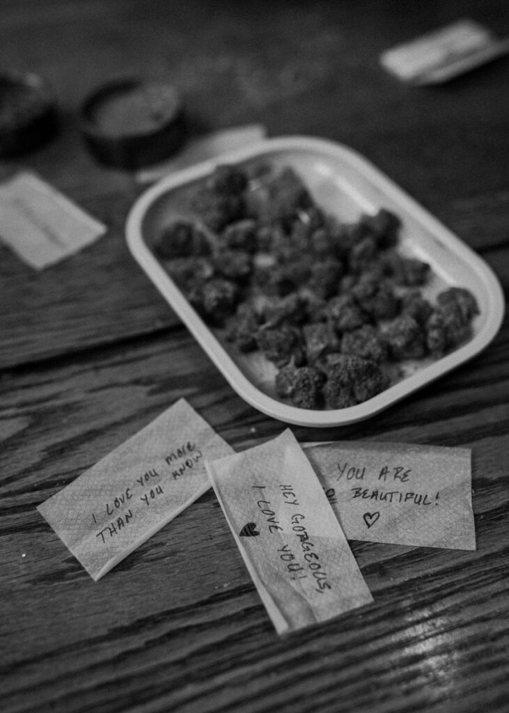 Black and white image of a home photoshoot focusing on cannabis buds on a plate with heartfelt handwritten notes like 'I love you' and 'You are beautiful'