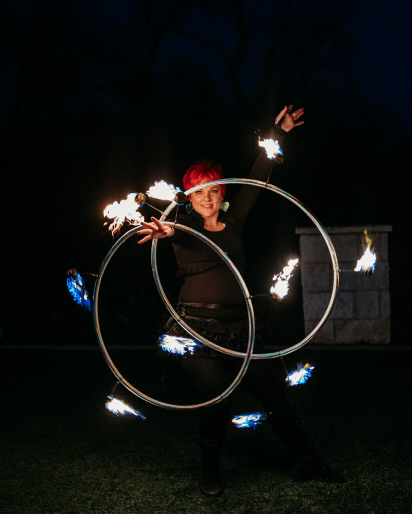 A fire artist performing with lit hoops at night, adding an element of daring spectacle to the wedding entertainment with her dynamic and fiery display
