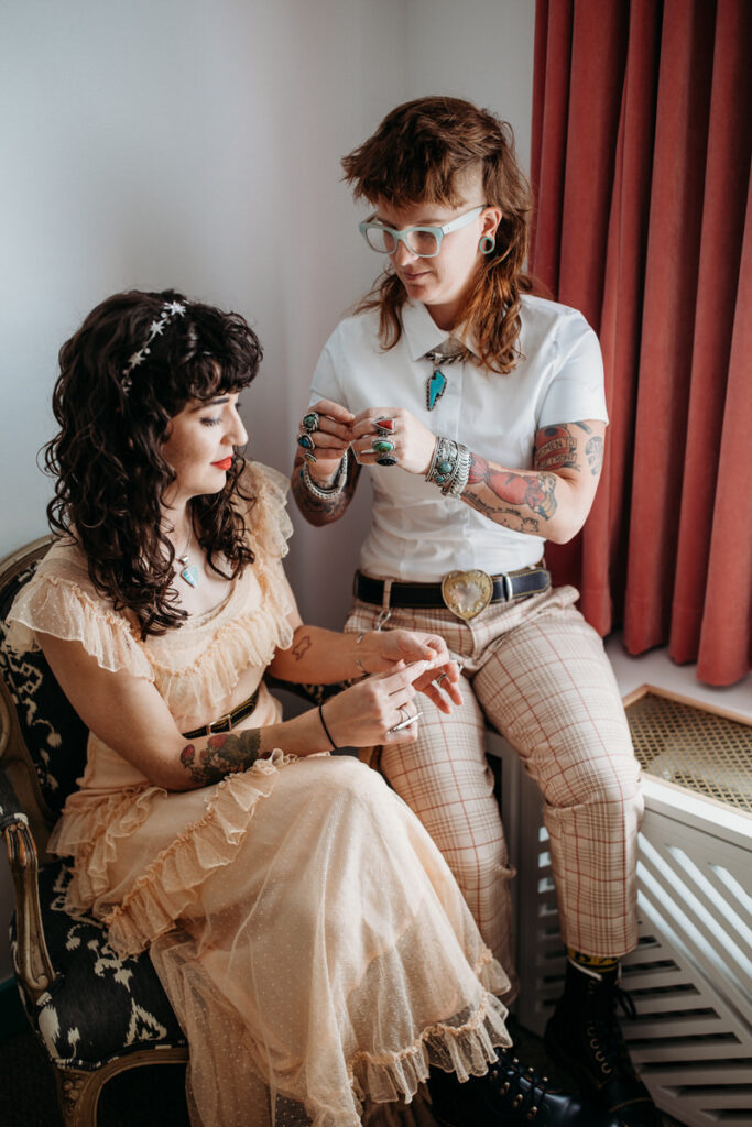 An intimate moment between a retro punk-styled wedding couple, sitting and sharing a drink, surrounded by vintage decor