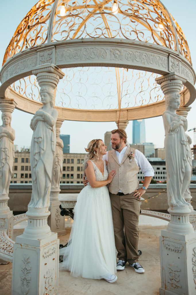 Newlyweds standing under an ornate gazebo adorned with statues, an elegant wedding venue in downtown Oklahoma City