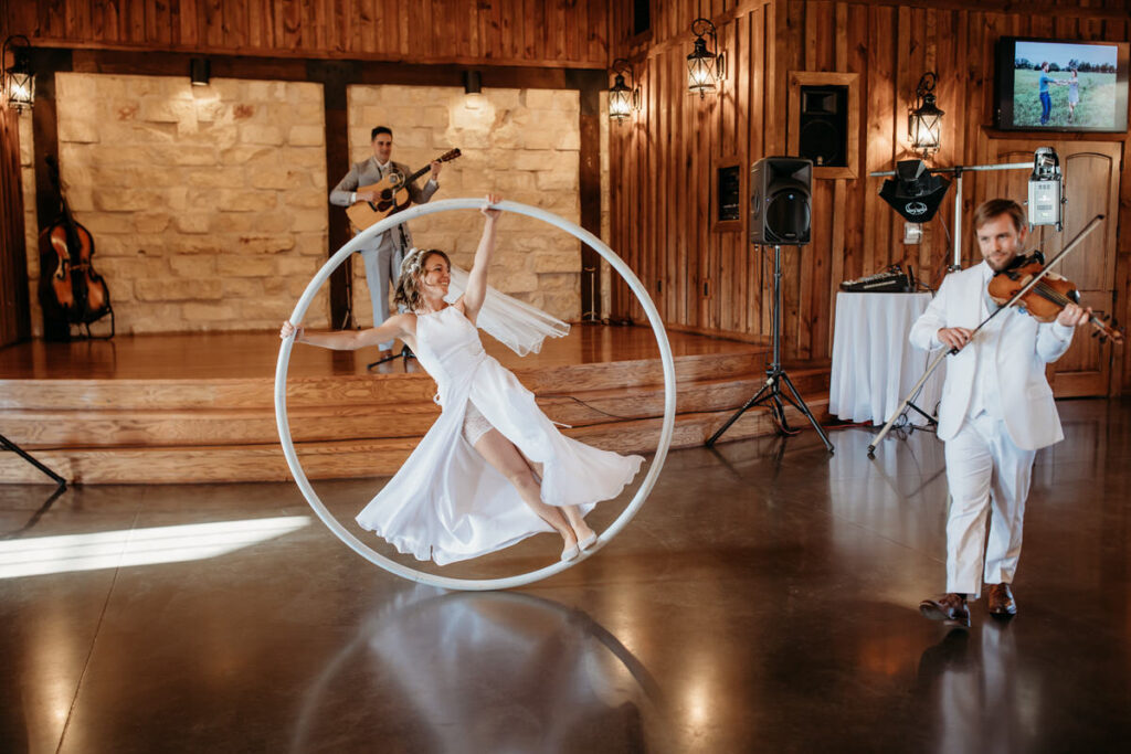 Bride performing an artistic routine on a Cyr wheel during the wedding reception, with live musicians playing in the background