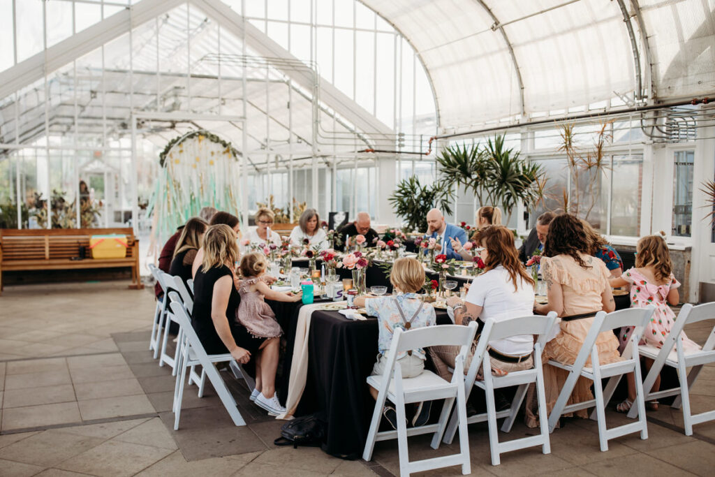 Guests seated at a conservatory reception surrounded by tropical plants, a unique greenhouse wedding venue in Oklahoma City